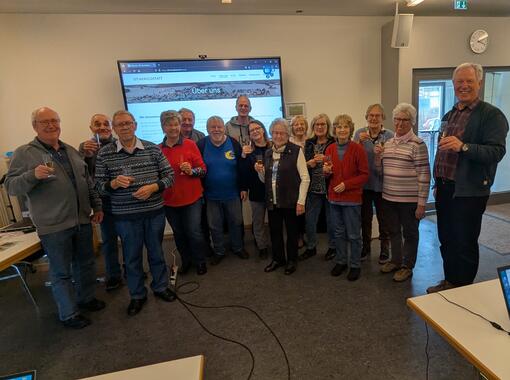 Die Gruppe der Ehrenamtlichen steht vor einem Monitor. Alle sehen fröhlich aus.