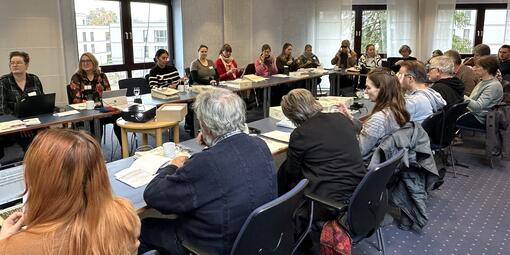 Ein Konferenzraum mit vielen Personen, die in U-Form an Tischen sitzen. Sie halten Simulationsbrillen in der Hand, die Seherkrankungen wiedergeben sollen.