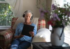 Frau sitzt im Sessel, liest am Tablet und hört Musik