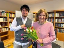 Zwei Personen (Frau C. mit Tulpen in der Hand und Bernd Josef Leisen). Beide stehen vor Bücherregalen in einem Raum im Albertinenhaus Hamburg. 