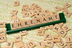 Verschiedene kleine Holzquadrate mit Buchstaben darauf. In der Mitte, innerhalb der vielen Quadrate, ist eine grüne, schmale Leiste aufgestellt. Sie zeigt das Wort "Ehrenamt".