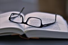 Eine Brille liegt auf einem aufgeschlagenen Buch.
